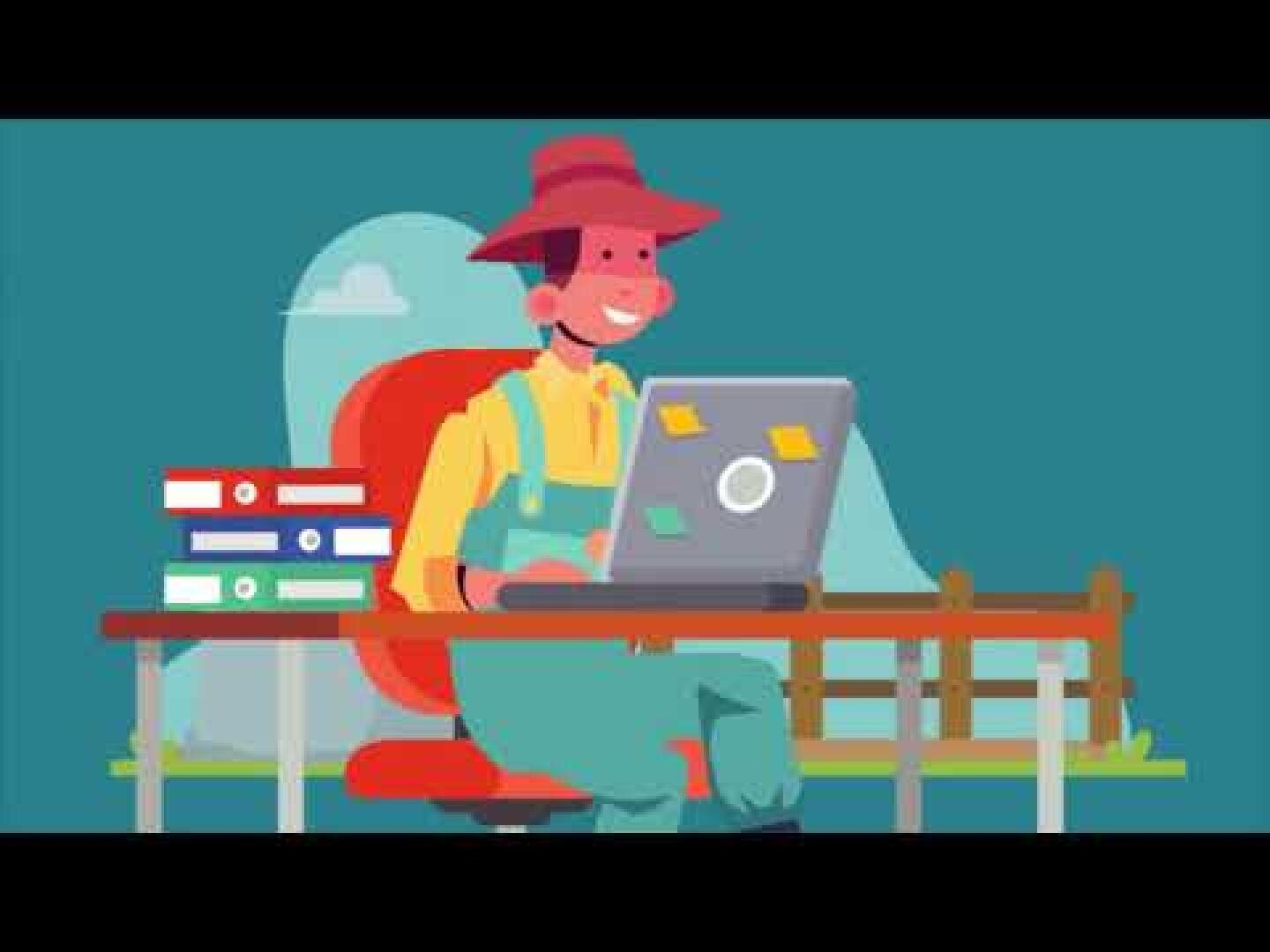 Ein lächelnder Bauer in Latzhose und Hut sitzt an einem Schreibtisch im Freien und arbeitet an einem Laptop. Auf dem Schreibtisch liegen Stapel von Ordnern, und im Hintergrund sind ein Zaun und Hügel zu sehen.