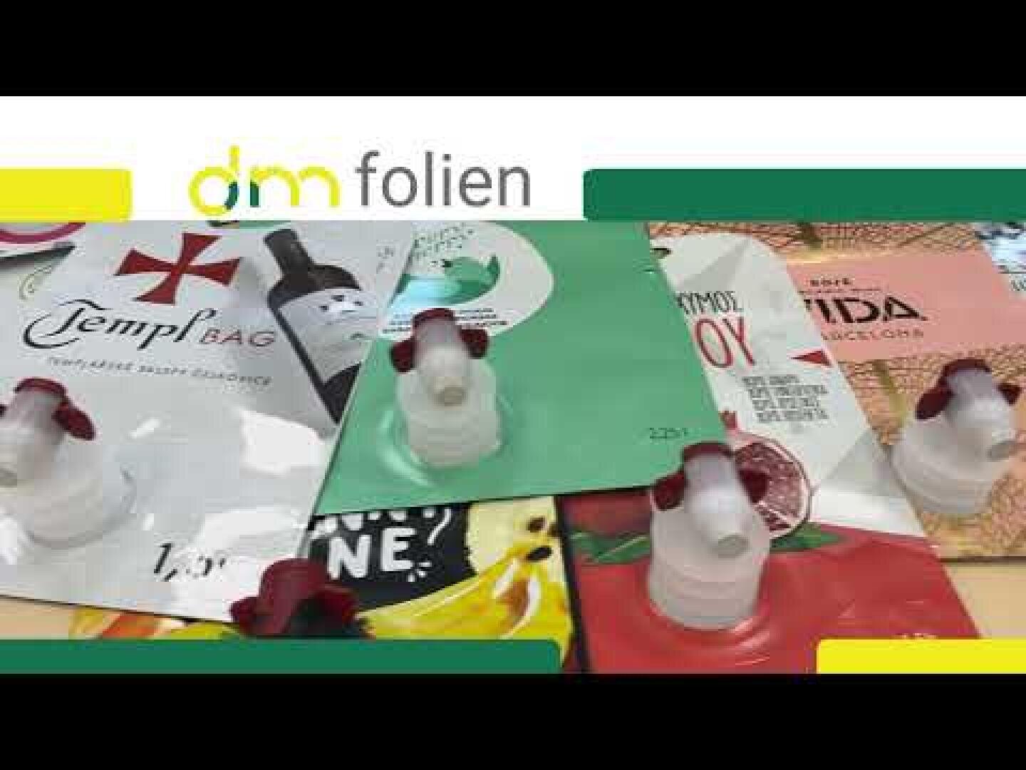 Verschiedene bunte, flexible Beutel mit Ausgießern sind auf einem Tisch ausgestellt, unter einem "dm folien"-Logo am oberen Rand des Bildes. Jeder Beutel hat ein anderes Branding und lebendige Designs.