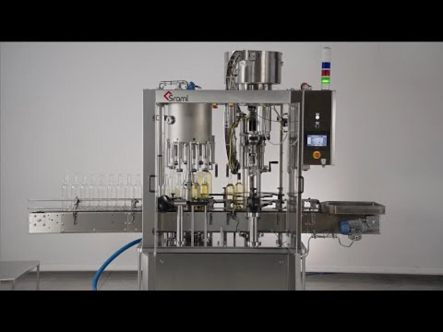 An automatic stainless steel bottling machine is shown in a factory hall. Several empty glass bottles are lined up on one side, with filled bottles in the middle. Control panels and hoses are visible.