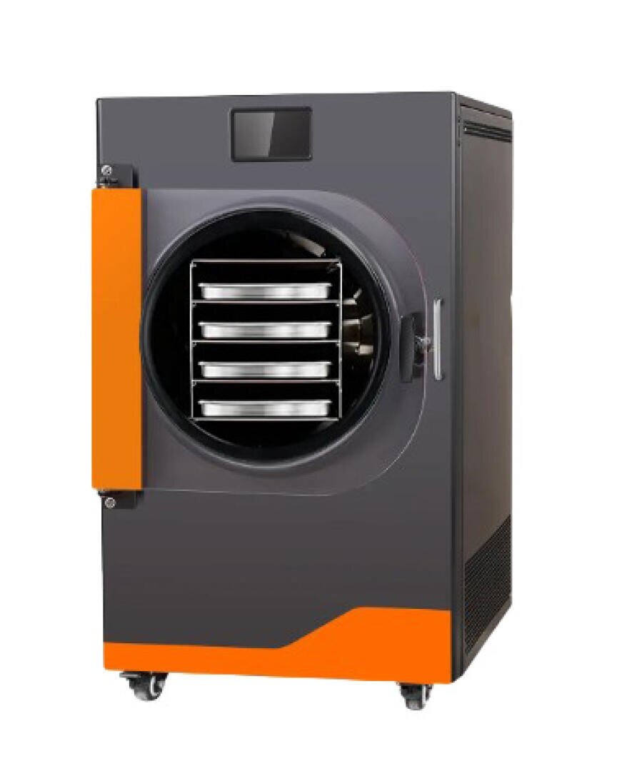 A modern, industrial freeze dryer with a gray and orange exterior, featuring a front door partially open to reveal four metal trays inside. The unit is on wheels for mobility.